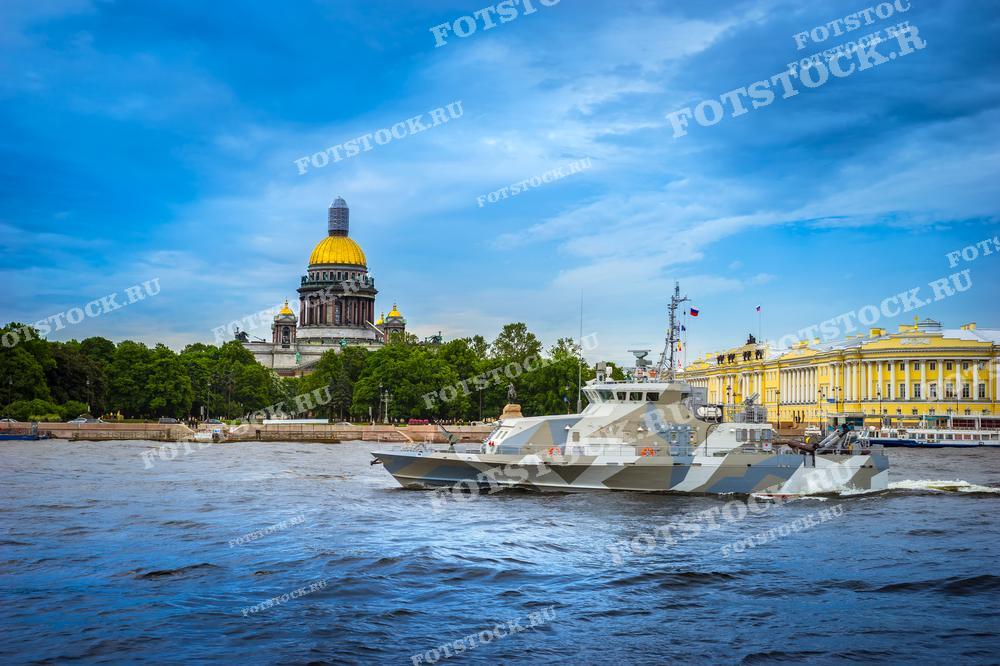 Фотография показывает Исаакиевский собор, одну из знаковых достопримечательностей Санкт-Петербурга, с видом на реку Неву, где плавают военные корабли. Этот снимок отлично подойдёт для использования в образовательных и культурных публикациях, а также может быть использован в туристических материалах для демонстрации исторического и современного облика города.